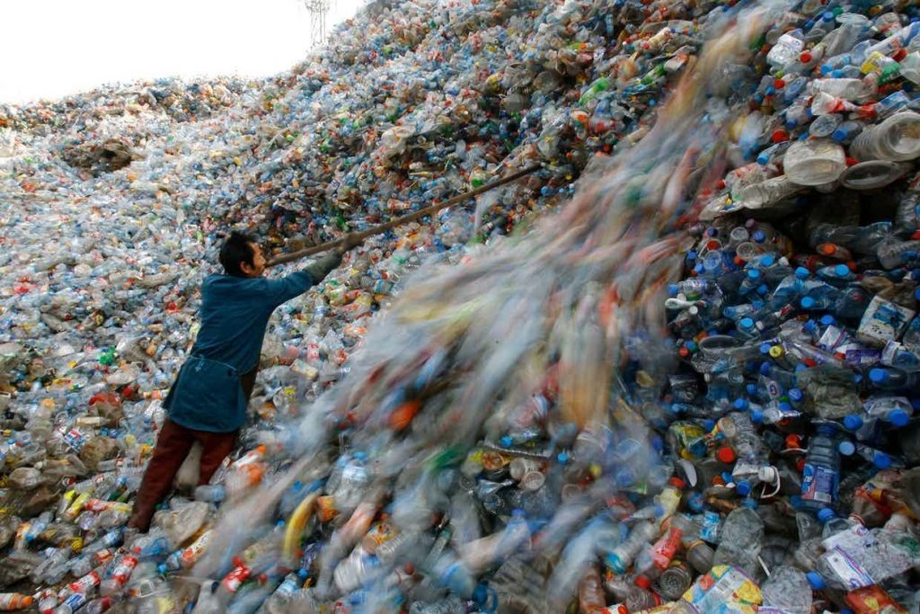 A worker is sorting plastic bottles that pile up into mountains